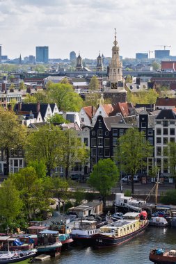 Amsterdam şehir manzarası: Tarihi mimari, kanal ve tekneler. Güneşli bir günde Avrupa seyahatlerinin, doğanın ve gayrimenkullerin sergilendiği pitoresk bir şehir manzarası.