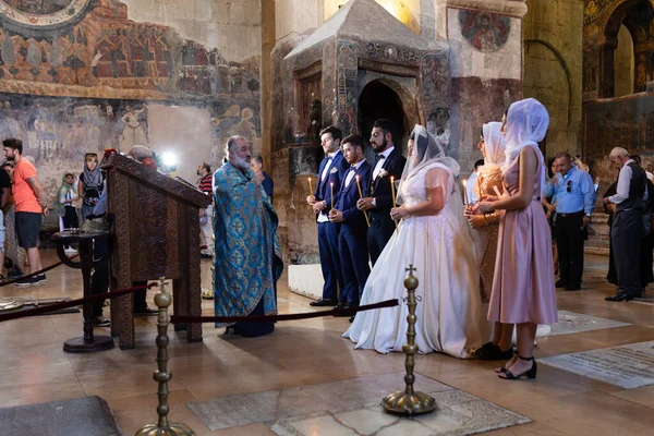 Mtskheta, Georgia-- 3 Ekim 2018: Eski bir kilisede geleneksel Ortodoks düğün töreni. Rahip, gelin ve damadın önünde duruyor tarihi taş duvarların yanında mumlar tutuyor..