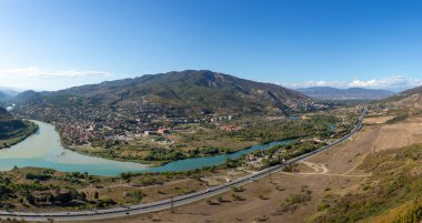 Mtskheta 'daki Aragvi ve Kura nehirlerinin kesişiminin panoramik manzarası. Manzarada trafiği ve tarihi kenti olan bir otoyol yer alıyor..