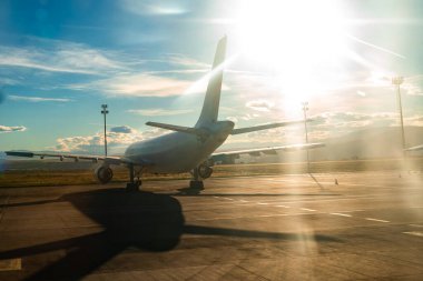 Gün doğumunda havaalanı pistinde parketmiş bir yolcu uçağının çarpıcı arka plan görüntüsü. Alçak güneş güçlü bir ışık ve karanlık bir gölge yaratır.