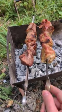 Mangalda ızgara et şişi çevirme ve dışarıda sıcak kömürlerin üzerindeki yapıyı kontrol etme videosu.
