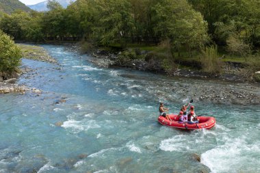 Pasanauri, Georgia- 2 Ekim 2018: Bir grup insan, Gürcistan 'daki yoğun yeşil orman ve dağlarla çevrili, hızlı, turkuaz mavisi Aragvi Nehri üzerinde beyaz su raftingi yapıyor..