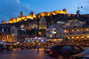 Aydınlatılmış Narikala Kalesi Gürcistan 'ın Tiflis kentinin hareketli sokaklarına ve restoranlarına bakıyor..