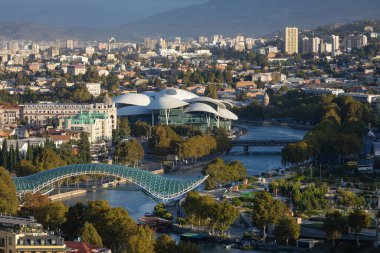 Mtkvari Nehri üzerindeki Barış Köprüsü ve Kamu Hizmetleri Salonu 'nun yer aldığı modern Tiflis şehir manzarasının panoramik görüntüsü.