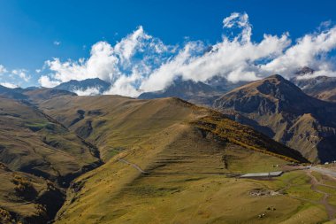 Gürcistan 'ın Kafkasya bölgesinde sonbahar çimenleri ve bulutlarla kaplı yuvarlanan dağ tepelerinin yatay manzarası..
