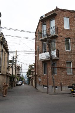 Tbilisi, Georgia- October 01, 2018: Vertical view of a narrow residential street in Old Tbilisi, Georgia, dominated by an old red brick apartment building and chaotic overhead power line wiring.
