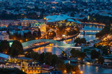 Mtkvari Nehri üzerindeki aydınlık Barış Köprüsü ve Gürcistan 'daki Kamu Hizmetleri Salonu' nun yer aldığı Tiflis şehir manzarası..