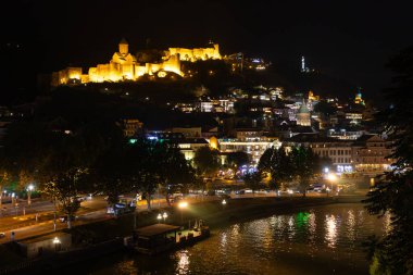 Gürcistan 'ın başkenti Tiflis' teki hareketli Mtkvari Nehri 'ne ve eski şehir setine bakan aydınlık Narikala Kalesi' nin göz kamaştırıcı gece manzarası.
