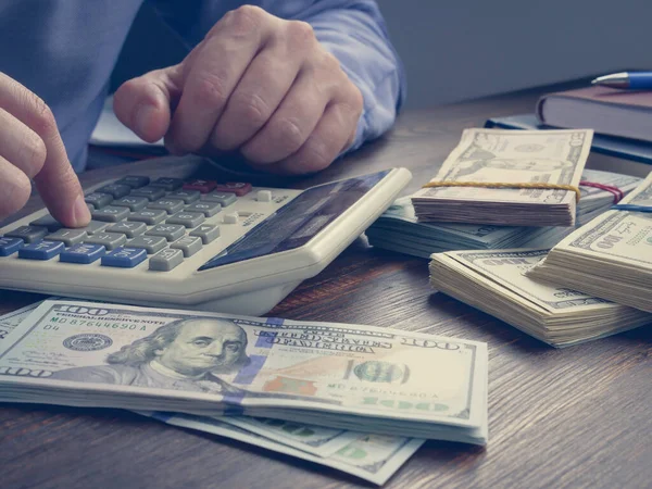 A man counts money on a calculator. Close-up of hands and a stack of cash.