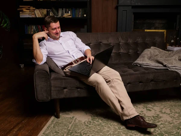 Sonriente hombre viendo vídeo en el ordenador portátil o charlando en línea mientras está sentado en el sofá en casa. — Foto de Stock