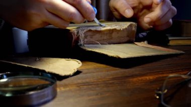 Eski bir kitabın kapağını yapıştıran ellerin yakın çekimi. Kitap tamiri ve restorasyonu bir hobi olarak.