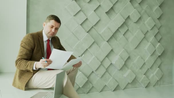A businessman in a suit works with a paper report and analyzes financial results with graphs. Empty space. — Stock Video