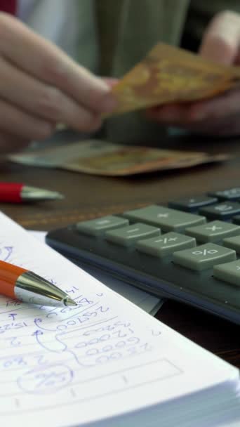 Un homme compte les billets en euros assis à une table avec une calculatrice. Vidéo verticale. — Video