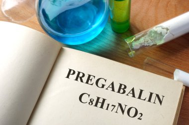 Book with Pregabalin  and test tubes on a table. clipart