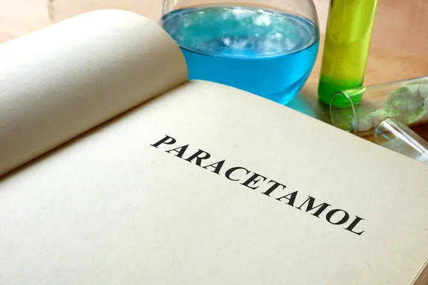 Libro con paracetamolo e provette su un tavolo . — Foto Stock