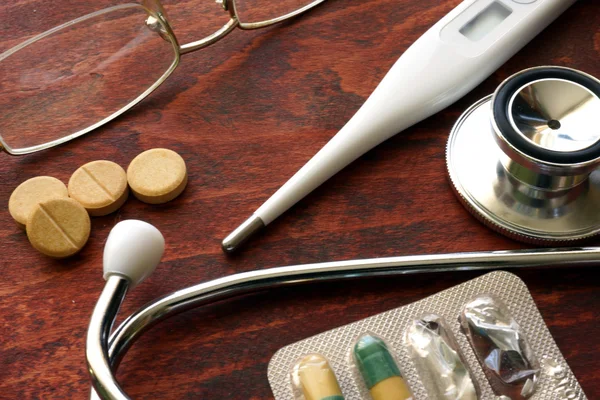 Stethoscope and thermometer with pills on a desk. Medical background. — Stock Photo, Image