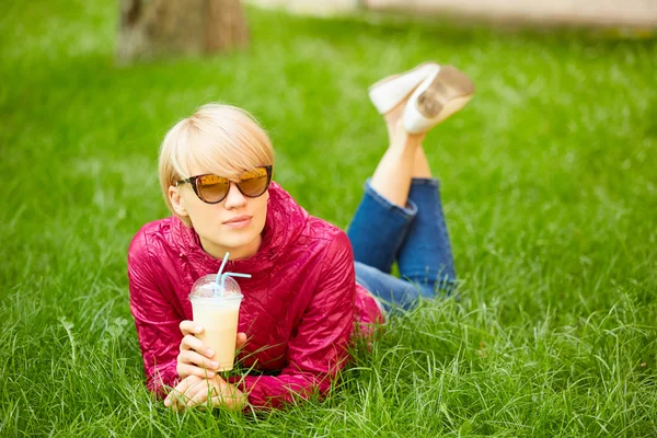 コーヒーを飲むと、草の上に横たわる美しい若い女性が楽しんでいます — ストック写真