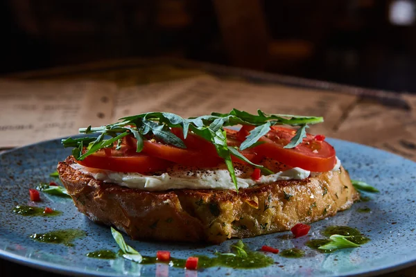 Bruschetta z serem, pomidorami i rukolą serwowane na niebieski płyta. — Zdjęcie stockowe