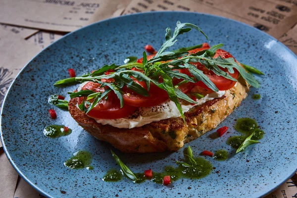 Bruschetta with cottage cheese, tomatoes and arugula served on blue plate. — Stock Photo, Image