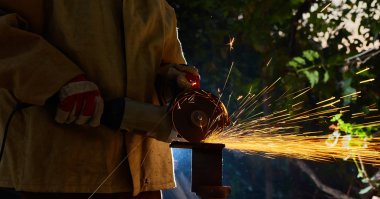 Öğütücüyle metal kesen bir işçi. Demir öğütürken kıvılcımlar