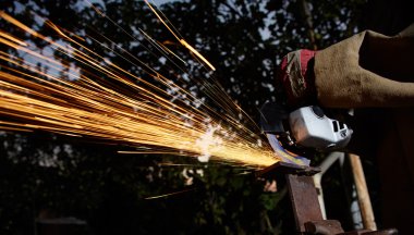 Öğütücüyle metal kesen bir işçi. Demir öğütürken kıvılcımlar