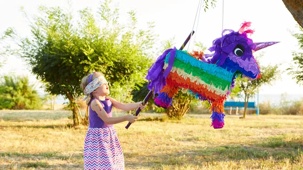Chica joven en una fiesta al aire libre golpeando una piñata — Foto de Stock