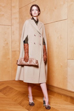 Kahverengi uzun paltolu, deri eldivenli, kontrplak arka planda seksi bir genç bayan.