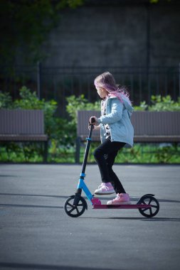 Gülümseyen küçük kız parkta scooter sürüyor. Metin için boş boşluk