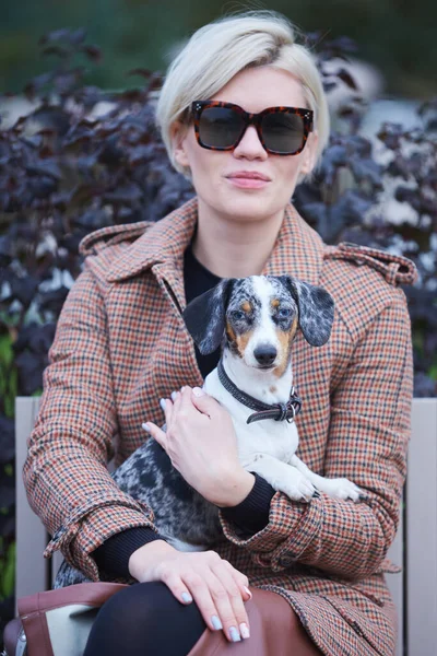 Állatgondozási koncepció. Egy fiatal nő, aki a tacskó kutyáját a karjaiban tartja a szabadban. Koncentrálj a kutyára. — Stock Fotó