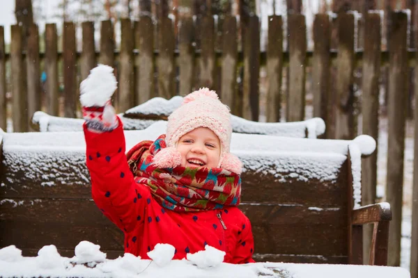 Menina de inverno jogando bola de neve na câmera sorrindo feliz se divertindo ao ar livre no dia de inverno nevando jogando na neve. Menina brincalhão bonito ao ar livre desfrutando primeira neve — Fotografia de Stock