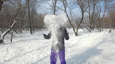 Beyaz ırktan, kalın elbiseli genç sakallı adam bir yığın kar kusar ve kurnazca gülümser. Kış mevsiminde parkta aktif dinlenme. Eğlence zamanı konsepti. Yavaş çekim.