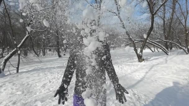Ung skäggig man av kaukasisk etnicitet i varma kläder kastar upp en hög med snö och ler försiktigt. Aktiv vila i parken under vintersäsongen. Kul tidskoncept. Långsamma rörelser. — Stockvideo
