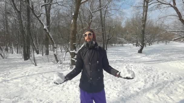 Homem barba jovem de etnia caucasiana em roupas quentes lança uma pilha de neve e sorri fofinho. Descanso ativo no parque na temporada de inverno. Conceito divertido de tempo. Movimento lento. — Vídeo de Stock