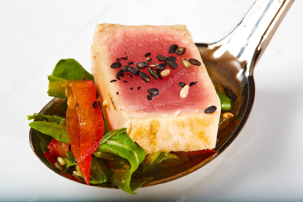 Close up of rare seared Ahi tuna slices with fresh vegetable salad on a plate. Shallow dof