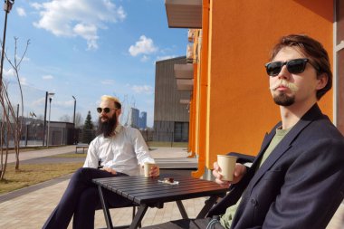 İki genç hippi bir kafede oturmuş sohbet ediyor ve kahve içiyor.