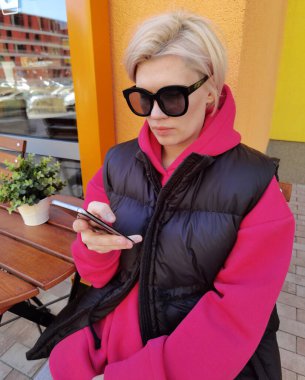 Yüksek teknoloji akıllı telefon kullanarak renkli bir şehir duvarına dayanan çekici genç bir kadının portresi.