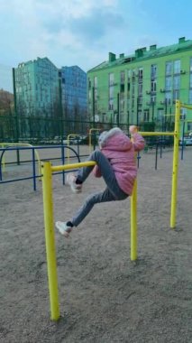 Küçük kız evin yakınındaki bir spor barında asılı duruyor. çocuk oyun alanında oynuyor