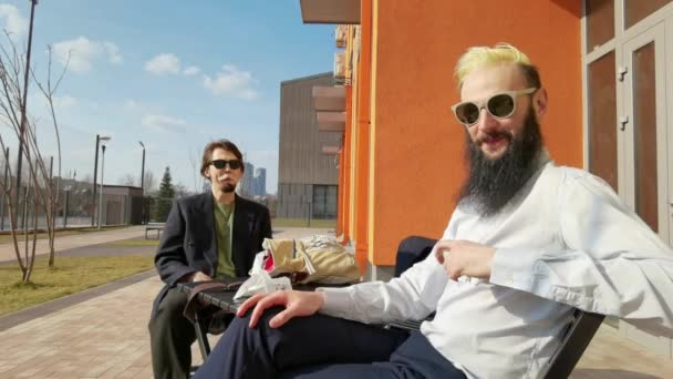 Dwóch młodych hipsterów siedzi w kawiarni i pije kawę uśmiechając się — Wideo stockowe