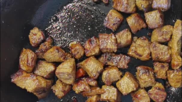 Pezzi di carne vengono fritti in olio frizzante in una padella calda. Colazione di addio al celibato, cibo facile da cucinare. Il cuoco mescola la carne con una spatola di legno. Macro, vista da vicino. Friggere carne, piano cottura. — Video Stock