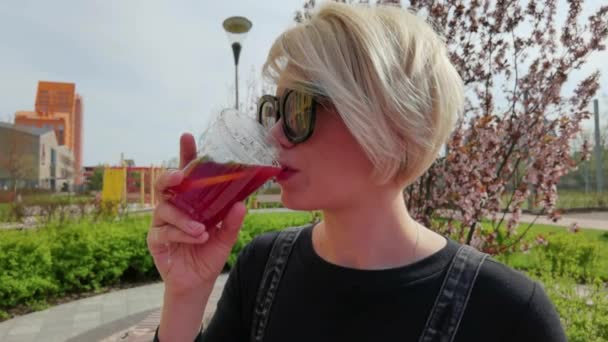 Jonge mooie glimlachende hippe vrouw. Model houden en drinken van verse cocktail smoothie drank in plastic beker. — Stockvideo