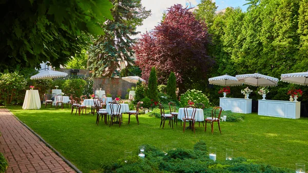 Runder Tisch mit weißem Tuch und Stühlen stehen auf einem grünen Rasen im Freien. — Stockfoto