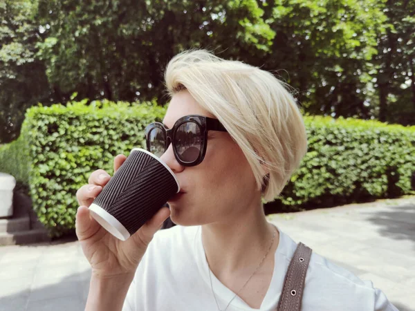 Linda chica hipster en gafas de sol con taza de café. Primer plano estilo de vida retrato al aire libre —  Fotos de Stock