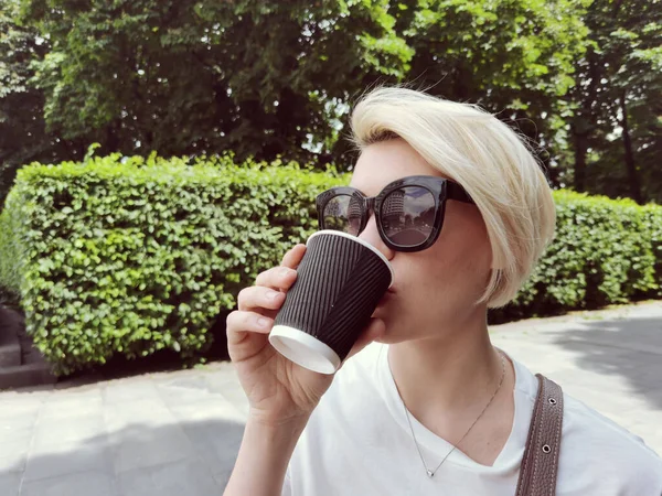Genç ve şık bir kadın parka gitmek için kahve içiyor. — Stok fotoğraf
