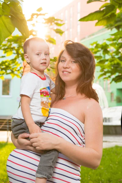 Riéndose joven madre embarazada jugando con su hijo en un hermoso jardín — Foto de Stock