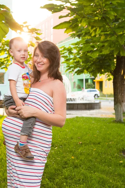 Śmiejąc się młoda matka w ciąży gry z jej syna w piękny ogród — Zdjęcie stockowe