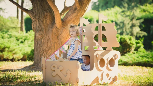 Boy and girl playing in a cardboard boat — Stock Photo, Image