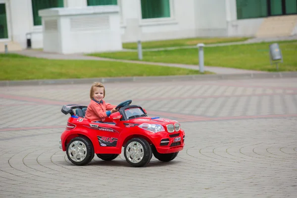 Beautiful little girl riding toy car in summer park — Stock Photo, Image