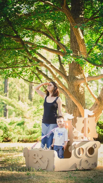 Mom and child playing in a cardboard boat. Summer day. — Stock Photo, Image