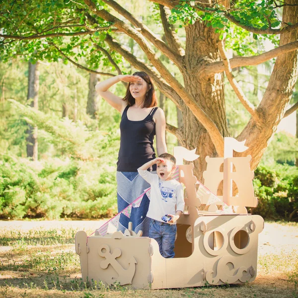 Mutter und Kind spielen in einem Pappboot. Sommertag. — Stockfoto