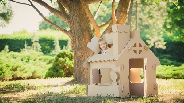 Girl playing in cardboard house at city park — Stock Photo, Image